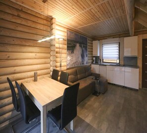 A cozy cabin interior with a wooden log wall, a dining area with a table and chairs, a sofa, a kitchen with cabinets and a window, and a painting on the wall. - Holiday Home in Rewal Near Sandy Beach (Rewal)