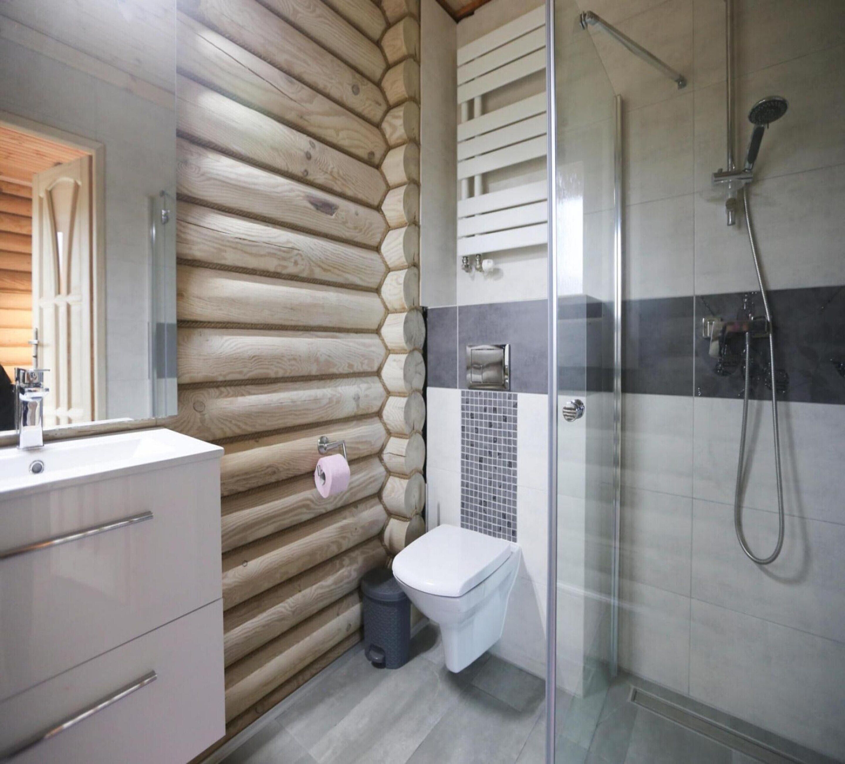 A modern bathroom with a wooden log wall, a glass shower enclosure, and a white sink.