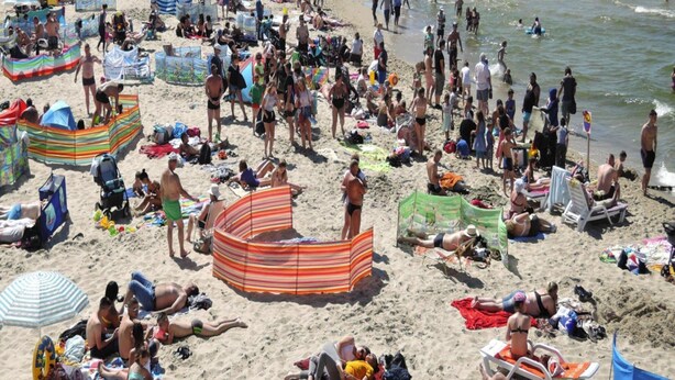 Ein überfüllter Strand mit vielen Menschen, Sonnenschirmen und Liegestühlen.
