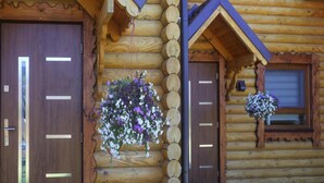 Eine Blockhütte mit zwei Holztüren, einem hängenden Blumenkorb und einem Fenster mit Blumen.'
