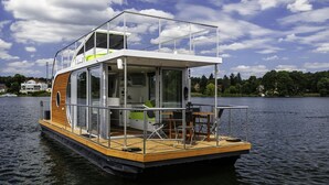 Una casa flotante con terraza, comedor y sala de estar con televisor y asientos.