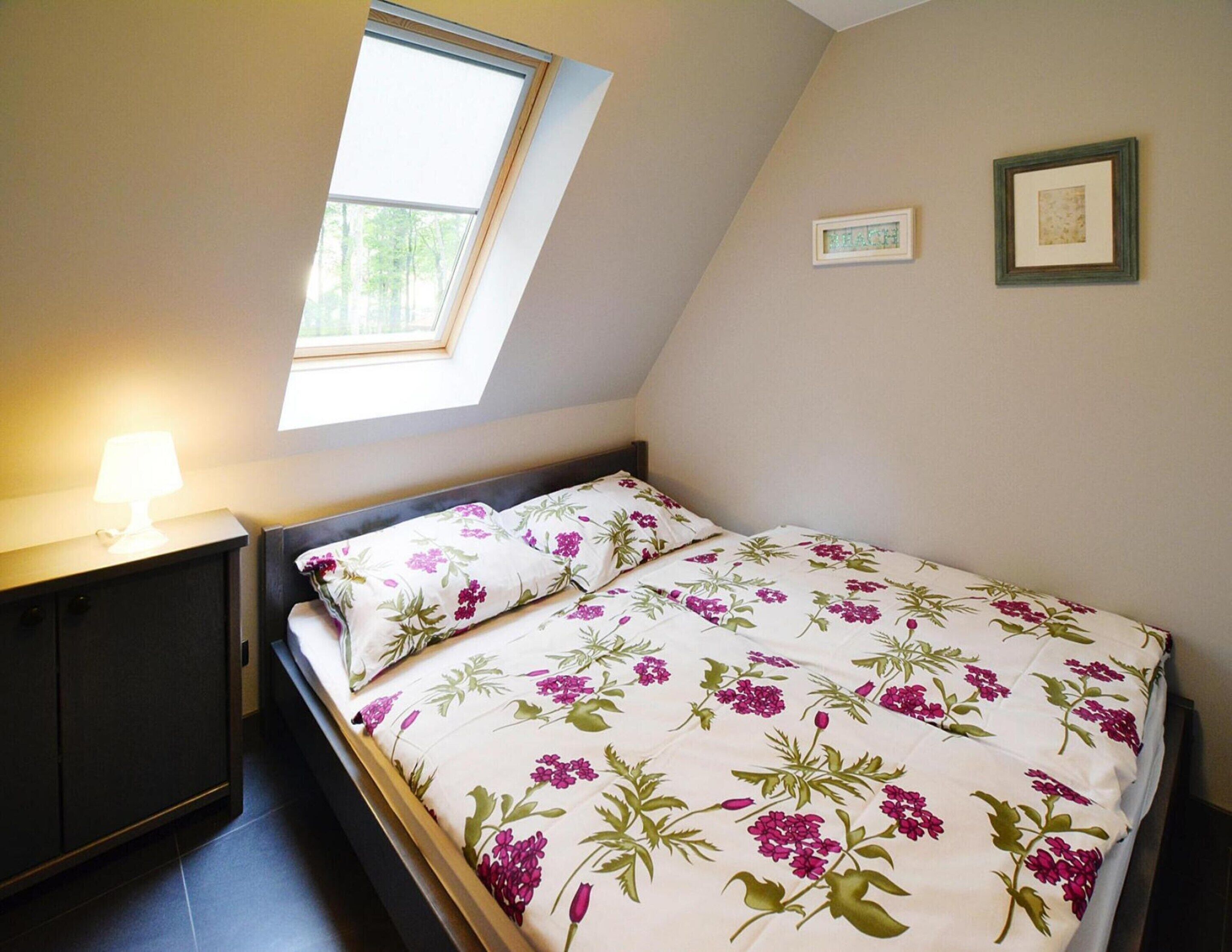 Une chambre à coucher avec un lit, une table de chevet, une lampe, une fenêtre et deux tableaux encadrés accrochés au mur.