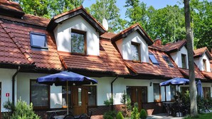 En række traditionelle huse med røde tegltage, udendørs siddepladser med parasoller, og en velplejet have.