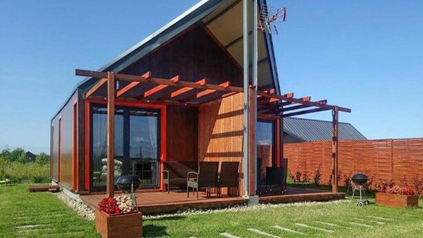Et moderne hus med skråt tag, store vinduer og en overdækket terrasse.