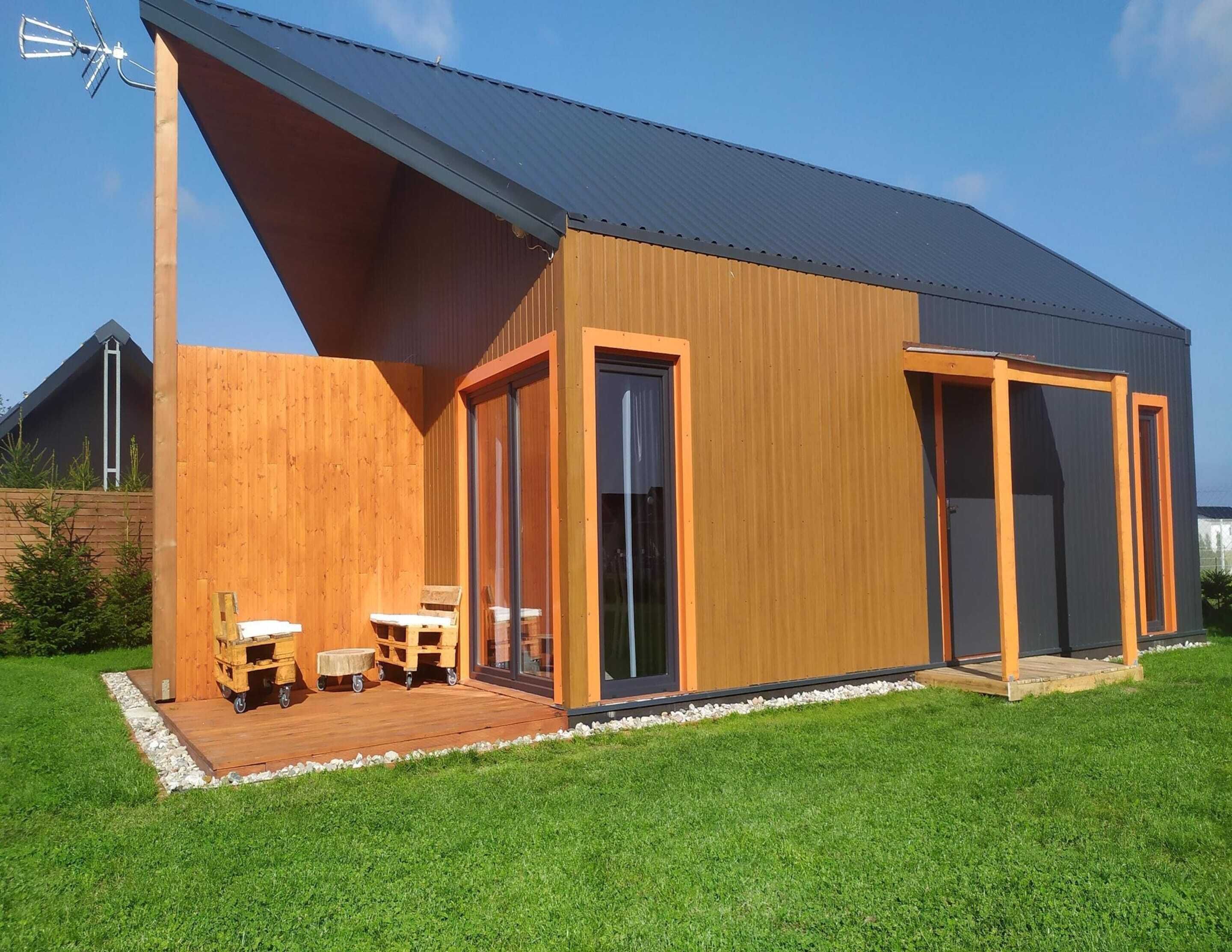 Ein modernes Haus mit Holzterrasse, großen Schiebeglastüren und einem Metalldach.