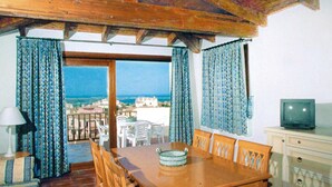 Une table à manger en bois avec des chaises, un téléviseur posé sur un meuble, et une vue sur la mer.