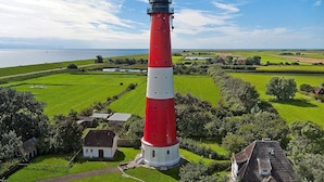 A red and white lighthouse with a clear view of the surrounding landscape, including green fields and a small building nearby. - Appartementhaus auf Pellworm (Pellworm)
