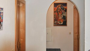 Un couloir avec une porte en bois sur la gauche et une porte cintrée surmontée d’un tableau.