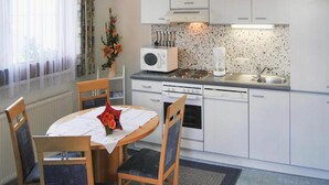 Une cuisine compacte avec des meubles blancs, un four à micro-ondes, une machine à café et un évier. On y trouve une table à manger avec des chaises et un vase de fleurs.