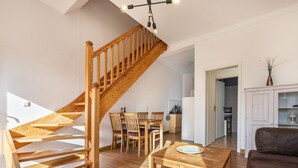A spacious living area with a wooden staircase, a dining table with chairs, a sofa, and a kitchen in the background. - Reihenhaus mit Wlan in Buchholz am Muritzsee (Buchholz)