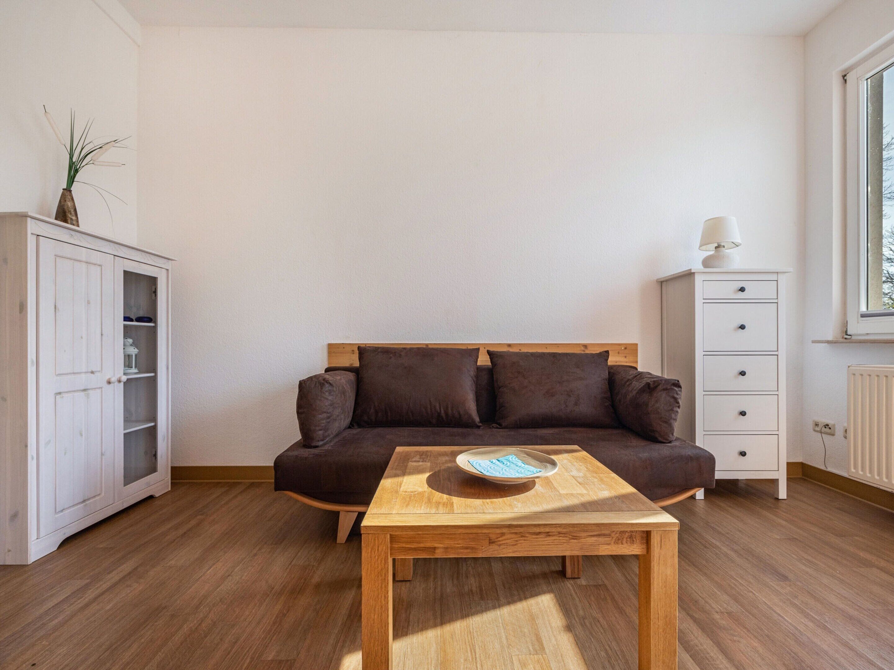 A living room with a brown sofa, a wooden coffee table, a white cabinet, and a window.