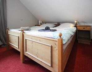 Ein hölzernes Bett mit Kopfteil, ein Nachttisch und ein Beistelltisch in einem Zimmer mit schrägem Dach.