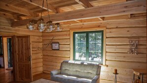 Ein gemütliches Blockhaus-Interieur mit Holzbalkendecke, einer Couch, einem Couchtisch und einem Fenster mit Blick auf Grünflächen.