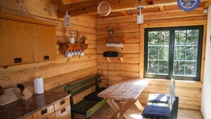 Eine Holzhütte mit einer Küche, inklusive Holztisch, Bank und Schränken.