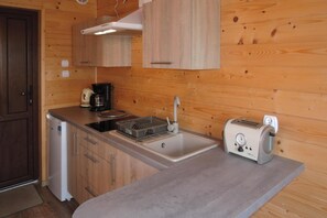 A compact kitchen with wooden cabinets, a built-in stove, a coffee maker, a toaster, and a sink. - Terraced House in Rewal Near Sandy Beach (Rewal)