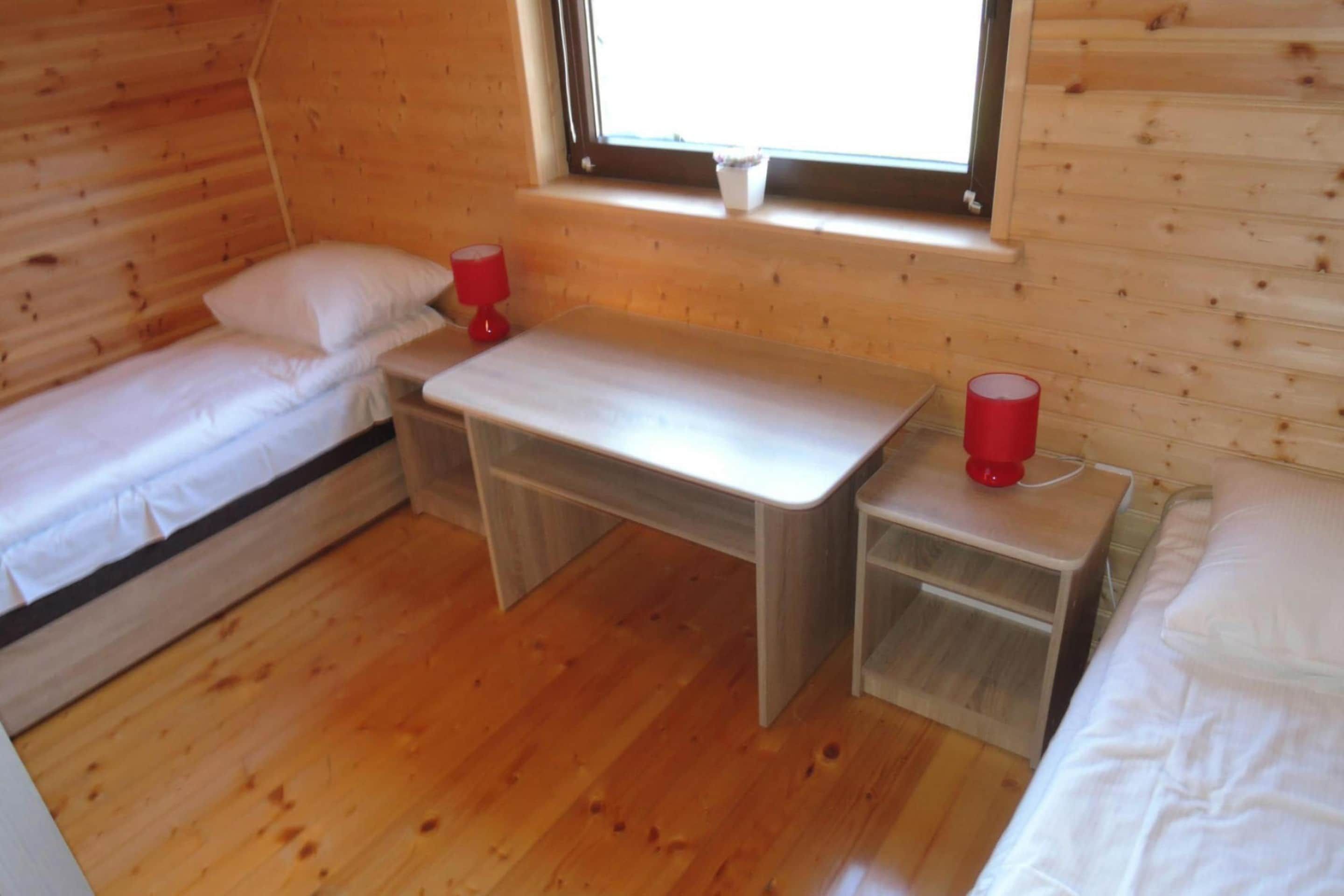 A small, cozy room with two single beds, a wooden desk, and a window.