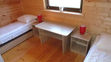 A small, cozy room with two single beds, a wooden desk, and a window.