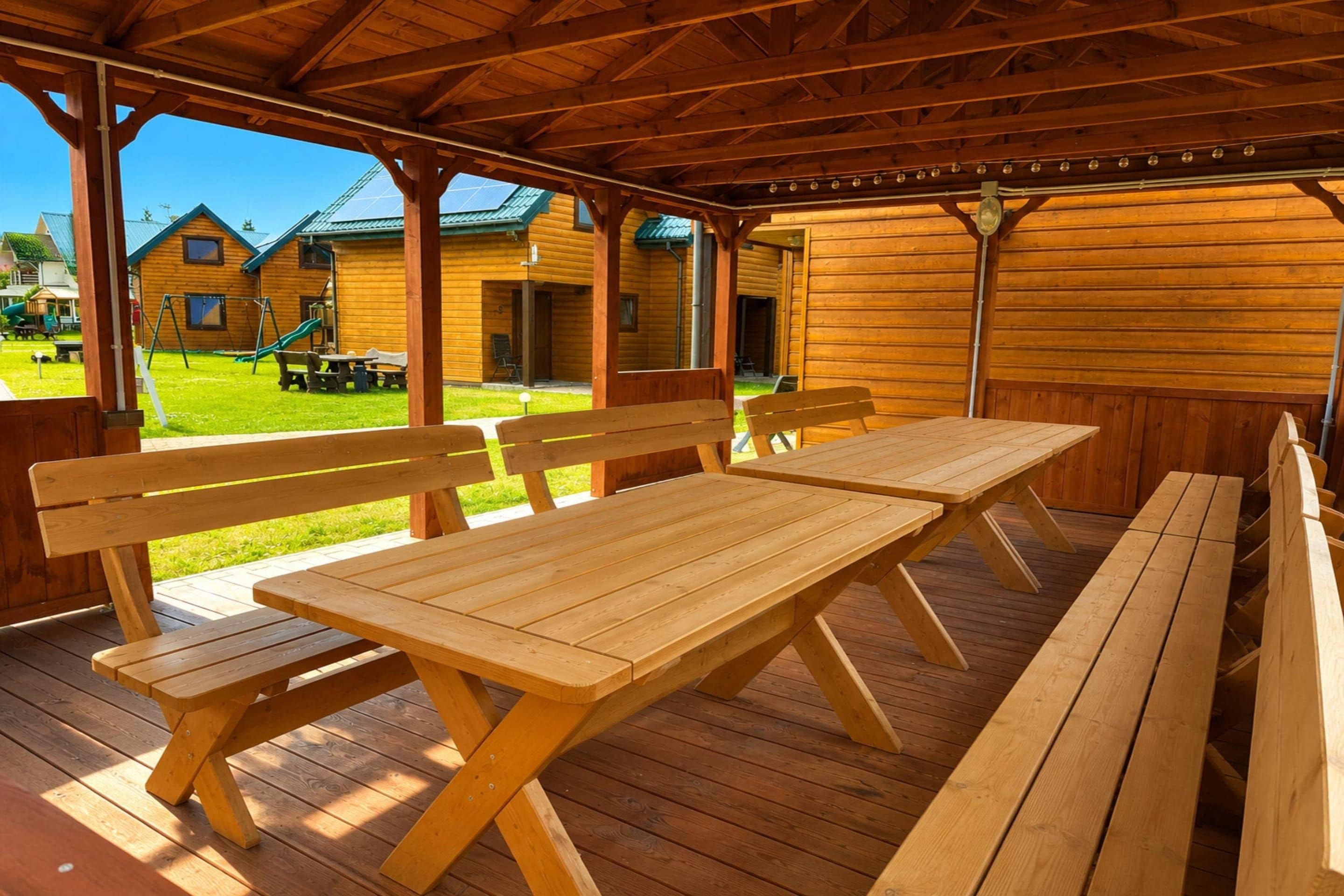 A wooden deck with picnic tables and benches, overlooking a grassy area with buildings in the background.