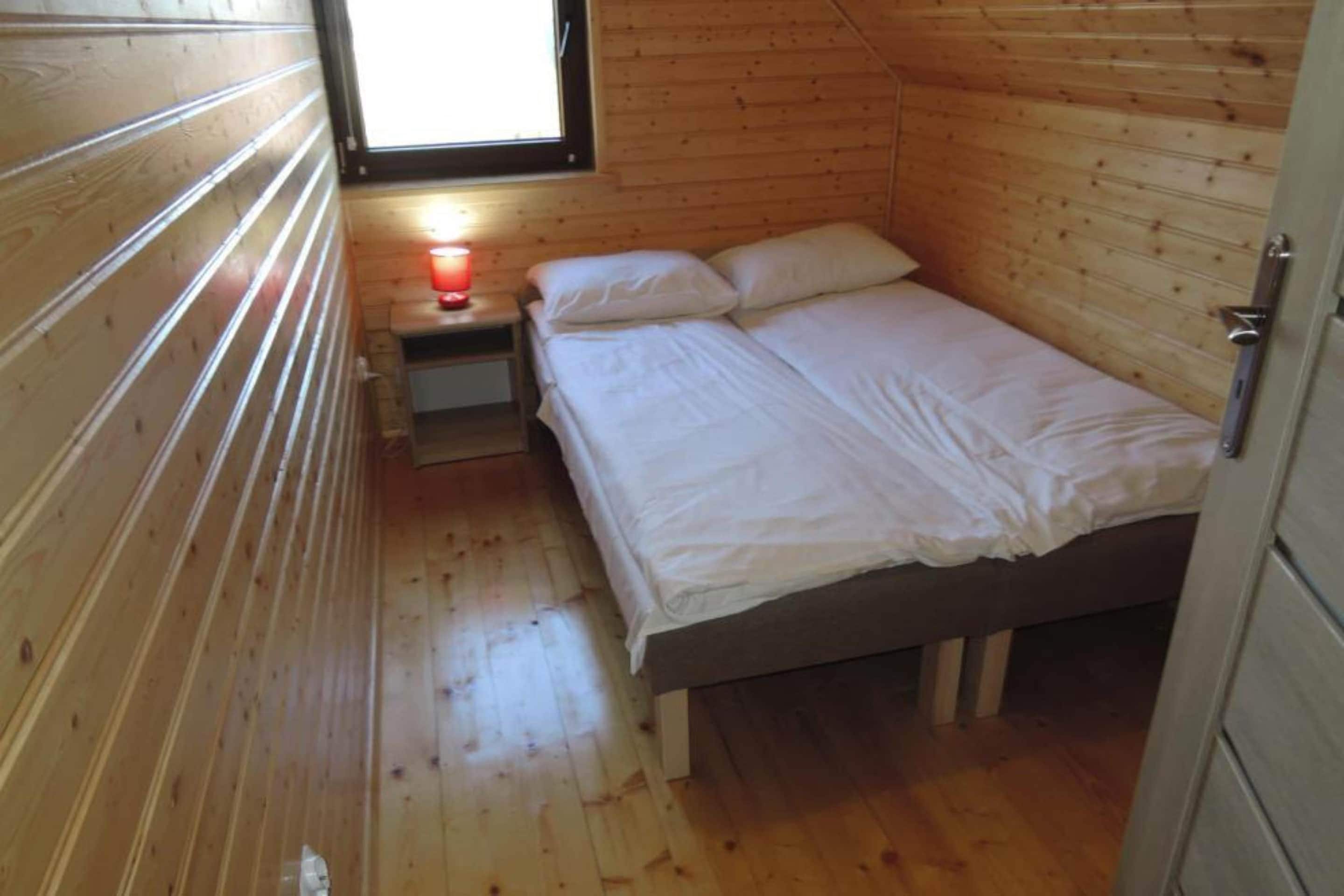 Una habitación pequeña con una cama individual, paredes de madera y una ventana.