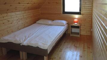 Una cama individual con estructura de madera en una habitación con paredes y techo inclinados de madera.