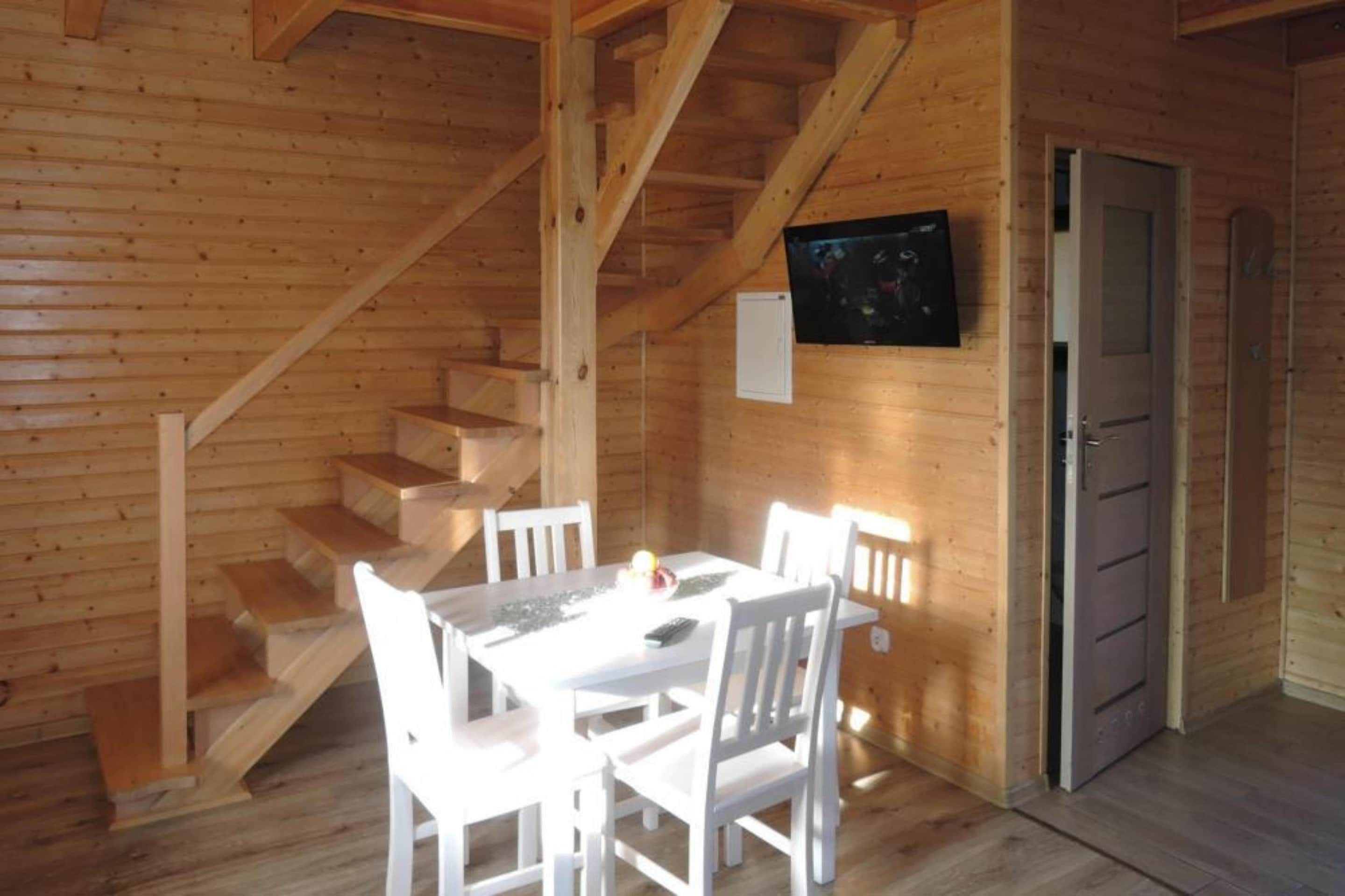 A wooden interior with a staircase, a dining table with chairs, and a door.