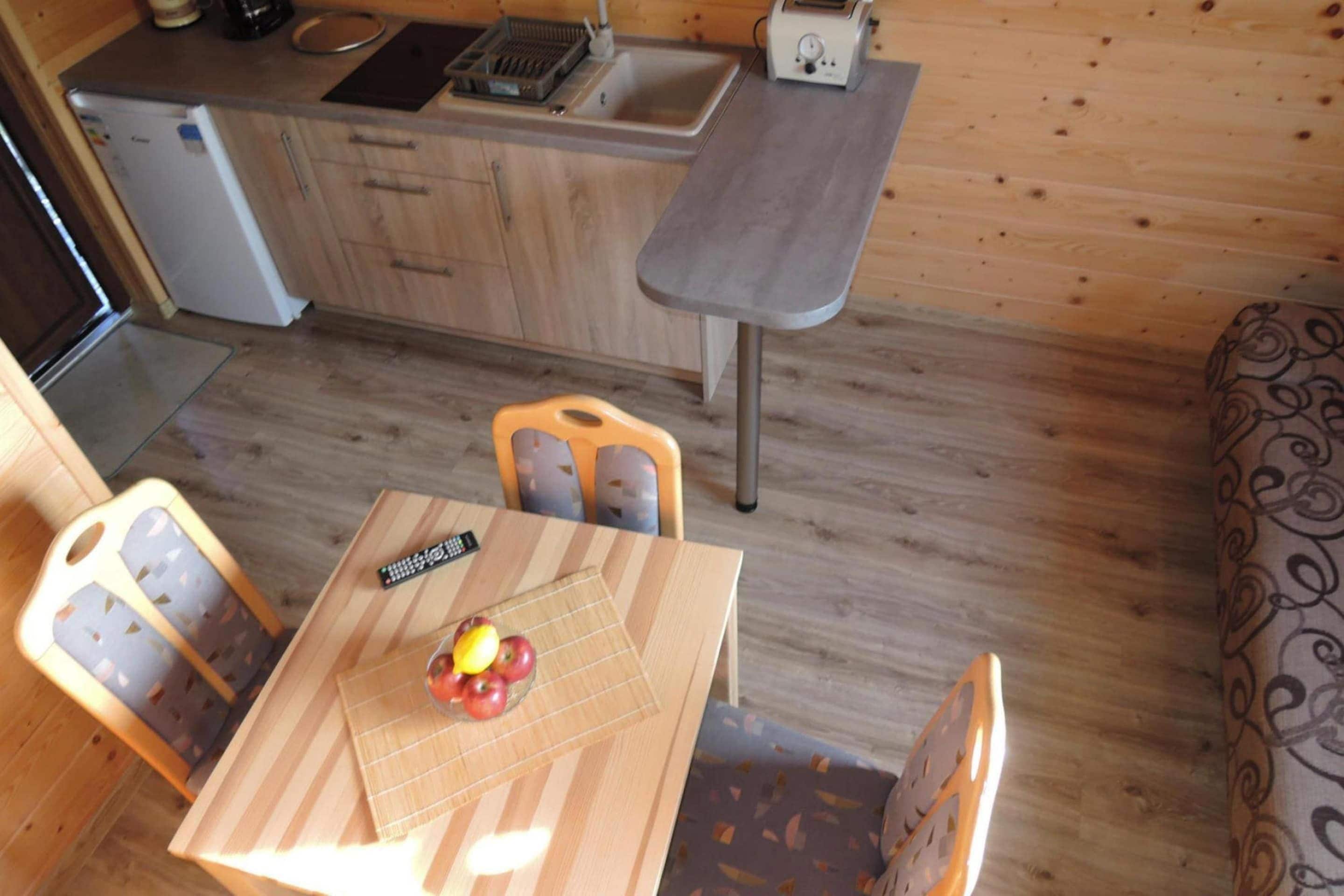 A compact kitchen with a sink, a toaster, and a refrigerator. There is a dining table with chairs and a remote control on it.