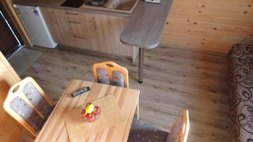 A compact kitchen with a sink, a toaster, and a refrigerator. There is a dining table with chairs and a remote control on it.