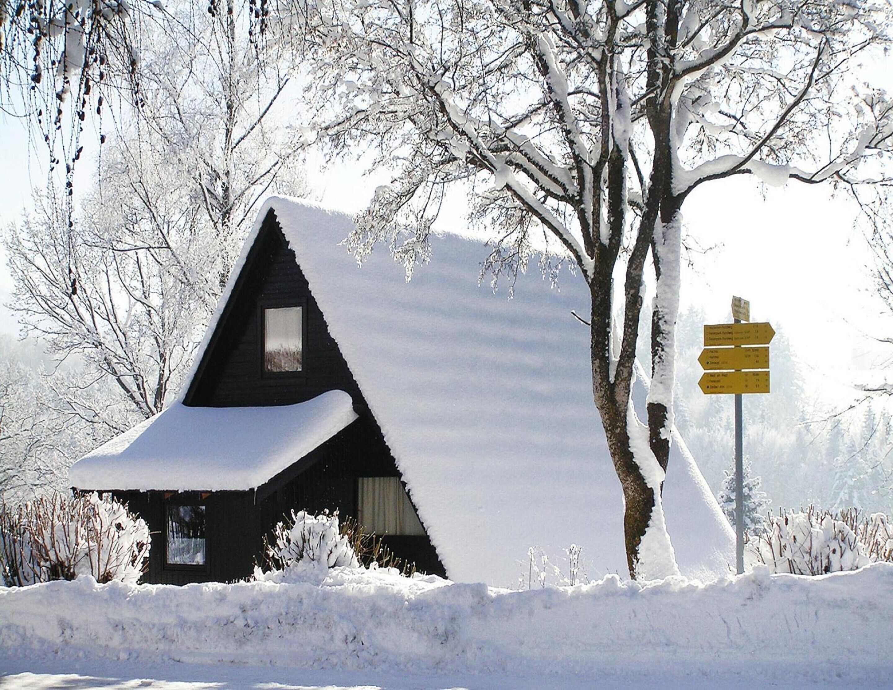 A snow-covered cabin with a triangular roof and a small window.