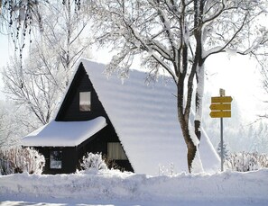 Una cabaña nevada con techo triangular y una ventana pequeña.