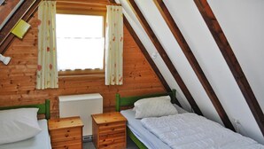 Une chambre confortable située sous les toits, avec deux lits simples, des tables de chevet en bois, un radiateur et une fenêtre agrémentée de rideaux à motifs floraux.