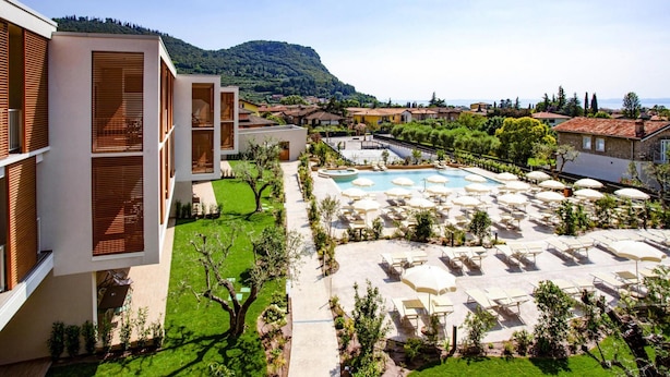 A hotel with a swimming pool, outdoor seating, and a view of a mountainous landscape. - Residence Olivo, Garda (Garda)
