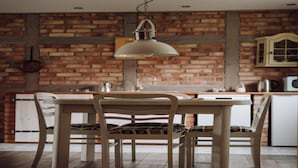 A kitchen with a brick wall, a hanging light fixture, a wooden table, and a chair. - Apartment in Gronowo Near Lake Siecino (Zlocieniec)