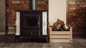 A wood-burning stove with a white mantel, a black chimney, and a wooden crate of logs beside it. - Apartment in Gronowo Near Lake Siecino (Zlocieniec)