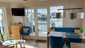 Een modern interieur met een houten vloer, een blauwe bank, een eettafel en een aan de muur bevestigde televisie.