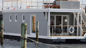 Een stilgelegen woonschip afgemeerd aan een steiger, met een overdekt dek, ramen en een reddingsboei.