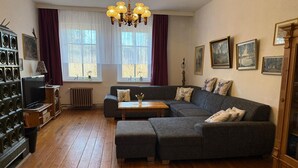 A living room with a sectional sofa, a wooden coffee table, a TV on a stand, a chandelier, and framed pictures on the wall. - Ferienhaus, Schorfheide (Schorfheide)