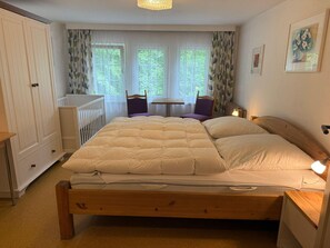 A bedroom with a bed, a crib, a chair, a table, and a window with curtains. - Ferienhaus, Schorfheide (Schorfheide)