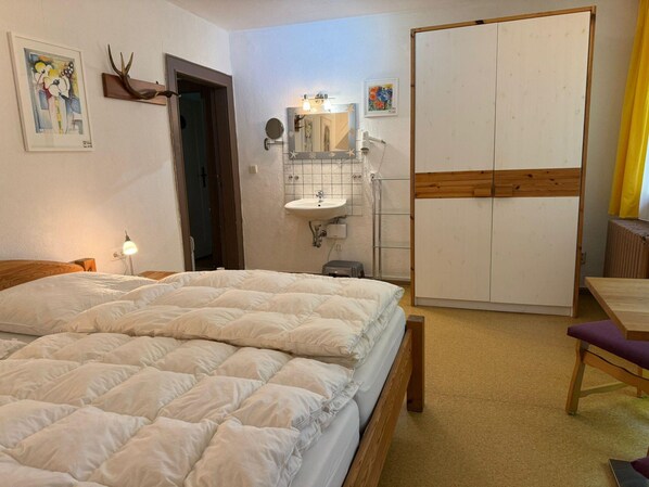 A bedroom with a bed, a bedside table, a mirror, a sink, and a wardrobe.
