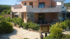 Una casa de dos pisos con fachada de piedra, un balcón y un patio con mobiliario exterior.
