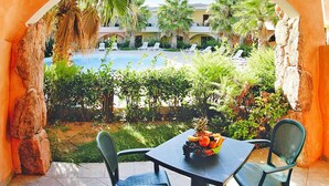 Un patio con mesa y sillas, un frutero y vistas a una piscina y palmeras.