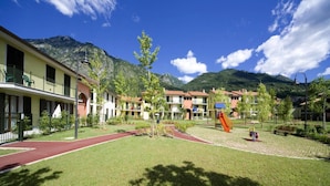 A hotel with a playground, a red running track, and a mountain backdrop. - Apartment in Porlezza With Lake View (Porlezza)