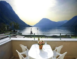 Una terraza con mesa y sillas que da a un lago con montañas al fondo.