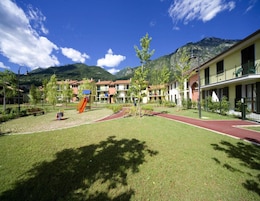Un patio con un parque infantil, una pista de atletismo roja y edificios con balcones.