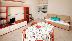 A compact living space with a dining table, a sofa, a kitchenette, and a TV on a shelf. - Residence Oasi del Viandante in Dervio (Dervio)