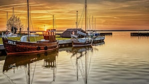 A calm harbor with boats docked, a small building, and a sunset in the background. - Ferienhaus, Fuhlendorf (Fuhlendorf)