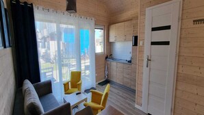 A compact living space with a sofa, two yellow chairs, a small table, a kitchenette, and a sliding door. - Single-story Holiday Homes, Pool, Playground (Mielno)