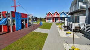 A playground with climbing structures and a slide, adjacent to a row of colorful houses with white railings. - Single-story Holiday Homes, Pool, Playground (Mielno)