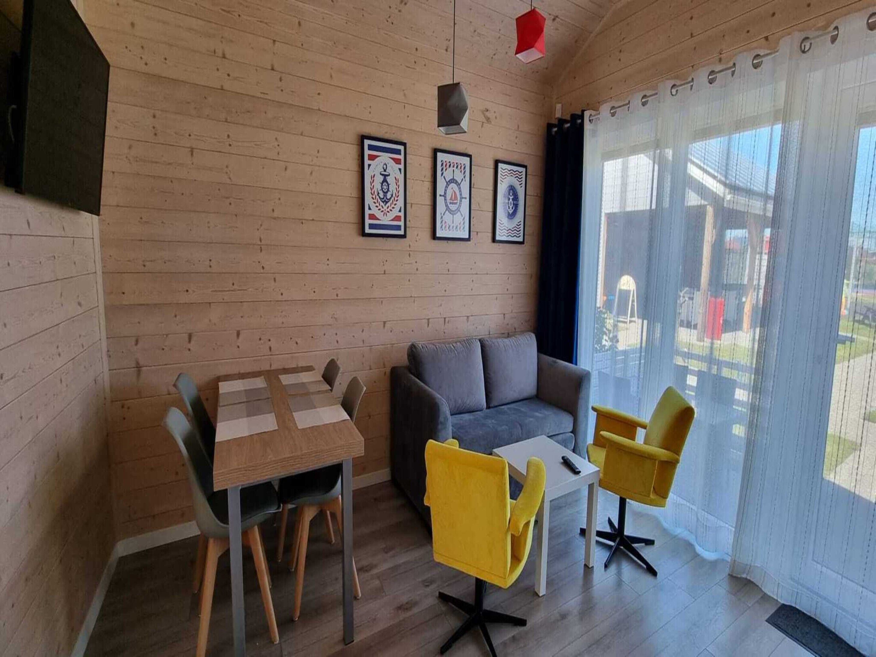 Ein gemütliches Zimmer mit Holzvertäfelung, einer Couch, einem Esstisch mit Stühlen und einem Vorhangfenster.