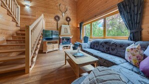 A wooden cabin interior with a staircase, a fireplace, a sofa, and a television.