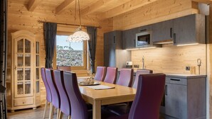 A wooden interior with a dining table and chairs, a kitchen area with cabinets, and a window with curtains.